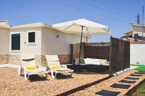 Limoeiro House villa in Sesimbra with beige loungers, umbrella, and wooden privacy fence on pebble terrace