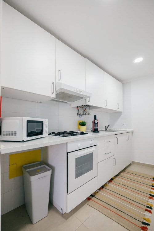 Modern kitchen in Limoeiro House villa at Tree House with white cabinets, gas stove, and colorful striped floor rug