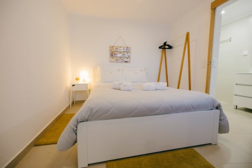 Modern bedroom at Tree House villa in Sesimbra with white bed, wooden coat racks, and warm lighting