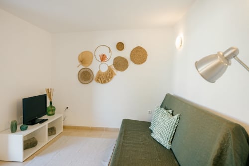 Modern living room at Tree House villa with green sofa, TV, decorative wall baskets, and contemporary lighting in Sesimbra