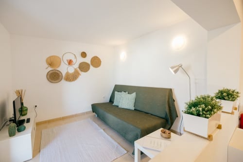 Modern living room at Tree House villa with green sofa, woven wall décor, potted plants, and natural lighting in Sesimbra,