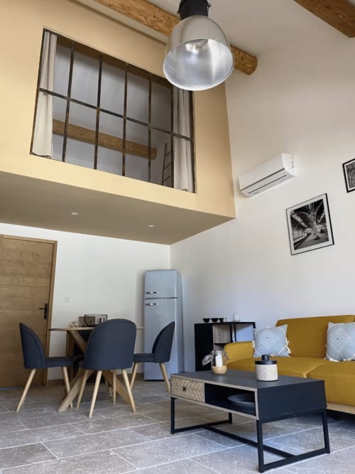 Séjour ouvert moderne avec canapé jaune, coin repas, kitchenette et réfrigérateur rétro bleu au gîte Mas St André