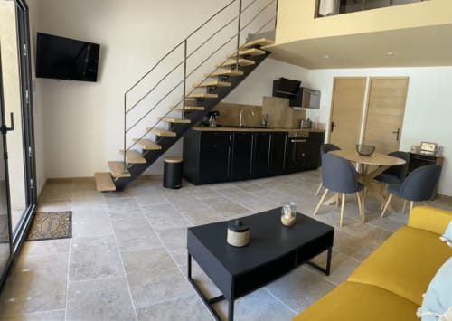Modern Provence cottage living room with black kitchen, staircase, yellow seating, and dining area at Mas St André