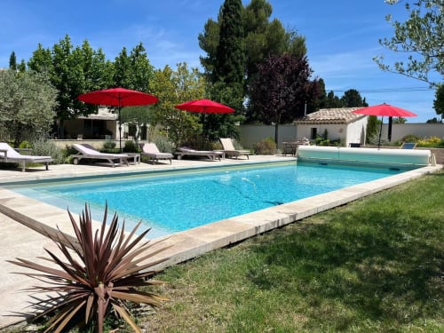 Rectangular swimming pool with turquoise water at Mas St André in Provence, featuring red umbrellas, loungers, and manicured