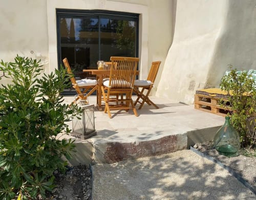 Sunny patio at Provence cottage with wooden chairs, potted plants, and large windows overlooking the terrace area.