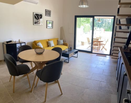 Modern open-plan living space at Mas St André cottage with dining table, yellow sofa, and doors opening to Provence garden