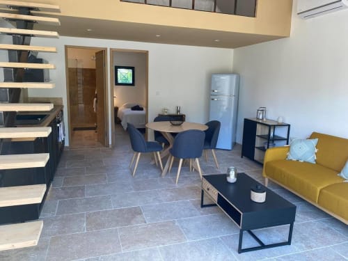Modern open-plan cottage interior at Mas St André with yellow sofa, dining table, kitchen, and bedroom at Gîtes Amandier in