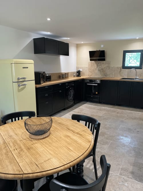 Modern kitchen with black cabinets, cream refrigerator, wooden dining table, and stone backsplash in Provence cottage
