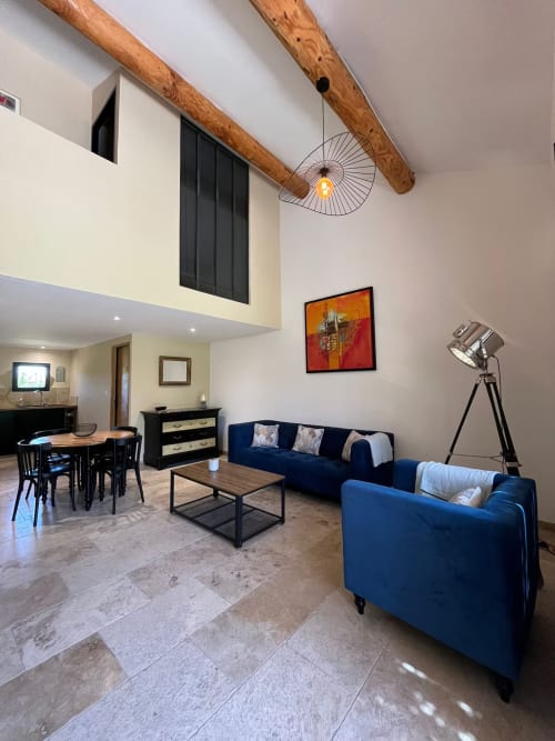 Salon de cottage provençal moderne avec fauteuils bleus, poutres en bois et coin repas au Mas St André