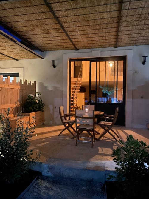 Evening patio at Mas St André cottage in Provence with dining table, chairs, and lit interior visible through glass doors