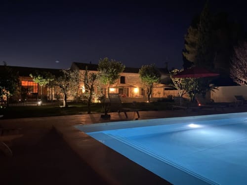 Nighttime view of Mas St André cottage in Provence with illuminated pool and terrace, trees and rustic stone building