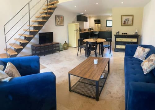 Modern open-plan living area with blue sofas, wooden dining table, kitchen, and staircase in Provence cottage