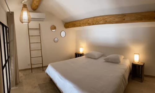 Bright bedroom in Provence cottage with white linens, exposed wooden beam, pendant lamp, and warm bedside lighting