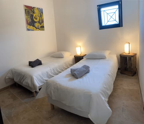 Twin beds with white linens in a bright bedroom at Mas St André cottage in Provence, with bedside lamps and artwork.