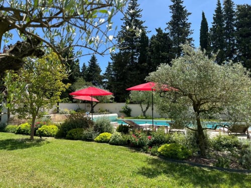 Sunny Provence garden at Mas St André with red umbrellas, pool, olive trees, and manicured lawn