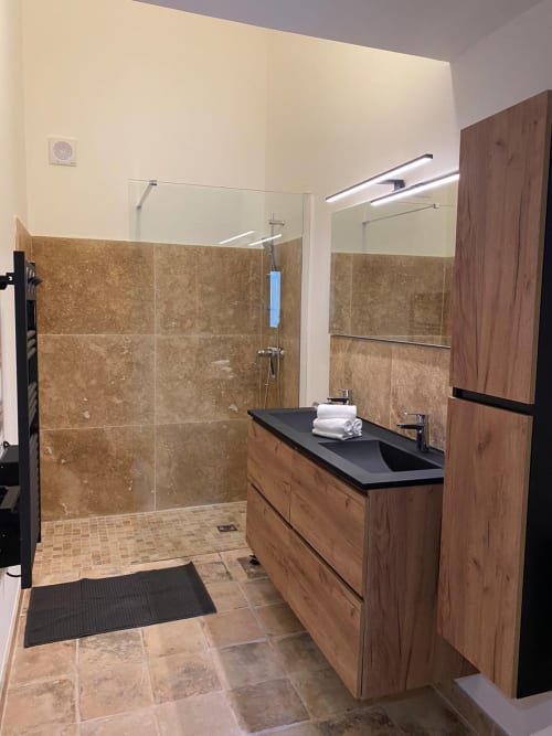 Modern bathroom in Mas St André cottage with wooden vanity, black sink, walk-in shower with travertine tiles, and heated