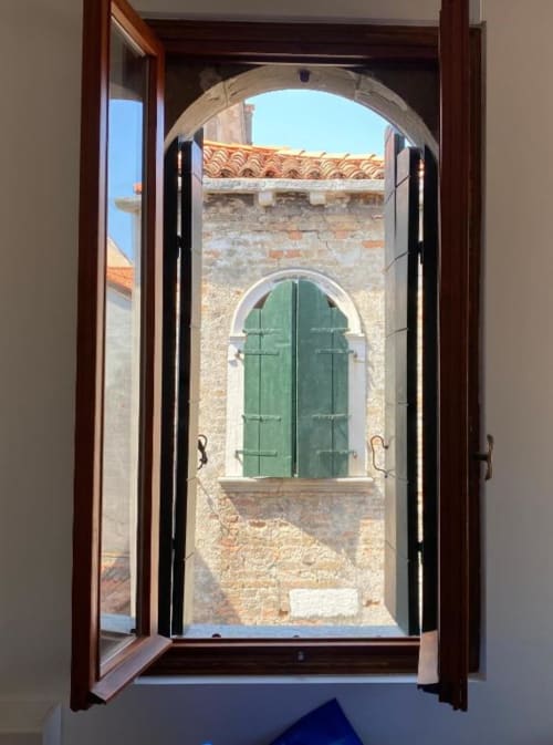 Vista attraverso le porte in legno aperto dell'architettura veneziana con finestra ad arco verde al Casanova Hideaway