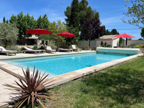Piscine étincelante avec parasols rouges et transats au gîte Mas St André à Saint-Andiol, France