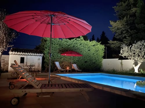 Vue nocturne de la piscine du Mas St André avec eau illuminée en bleu, parasols rouges, chaises longues et jardins luxuriants
