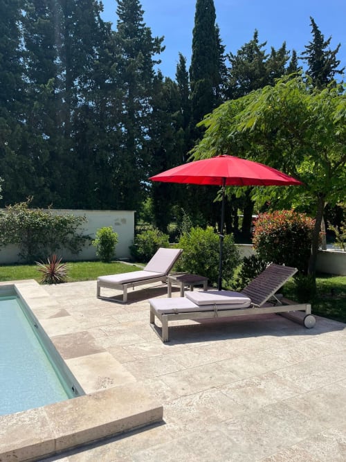 Élégante terrasse piscine au Mas St André à Saint-Andiol avec parasol rouge et transats donnant sur les jardins