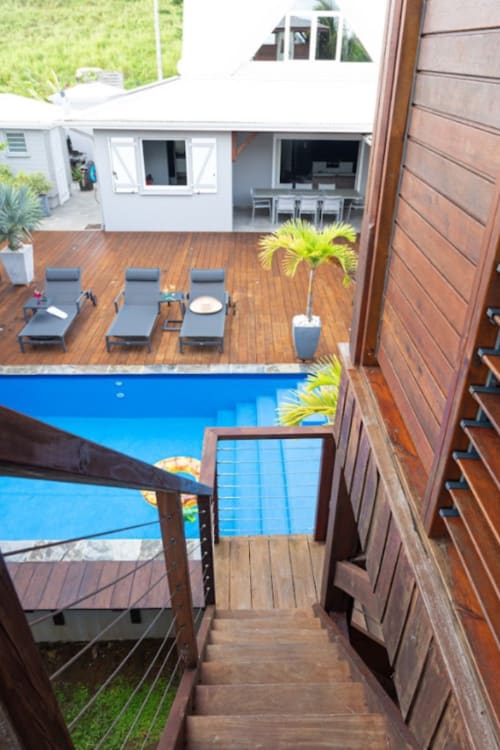 Vue aérienne de la terrasse piscine Paradise Location avec transats, terrasse en bois et villa moderne blanche à Fort-de-France
