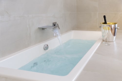 Vasca da bagno lussuosa a Bluemoon Sardegna riempita di acqua azzurra chiara, con moderno rubinetto cascata e set champagne