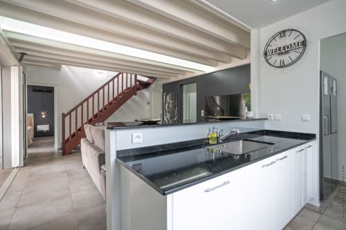 Modern villa kitchen with black granite counters, white cabinets, staircase, and welcome clock at Paradise Location