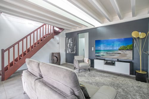 Modern villa living room with beige sofa, 65-inch TV showing beach scene, red staircase, and gray accent wall at Paradise