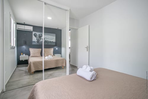 Modern villa bedroom in Fort-de-France with mirrored wardrobe, beige bedding, dark accent wall, and contemporary furnishings