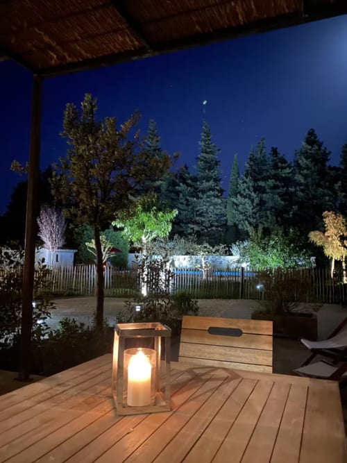 Twilight terrace at Mas St André with candlelit lantern, wooden bench, and coniferous forest backdrop in Saint-Andiol