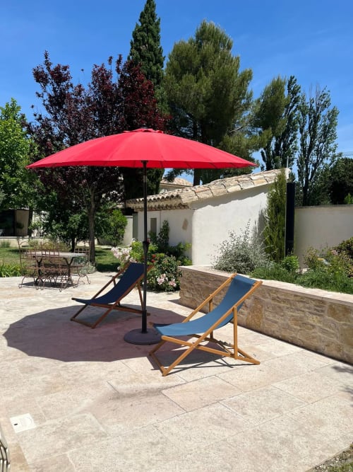 Red patio umbrella with blue deck chairs on stone terrace at Mas St André in Saint-Andiol, France
