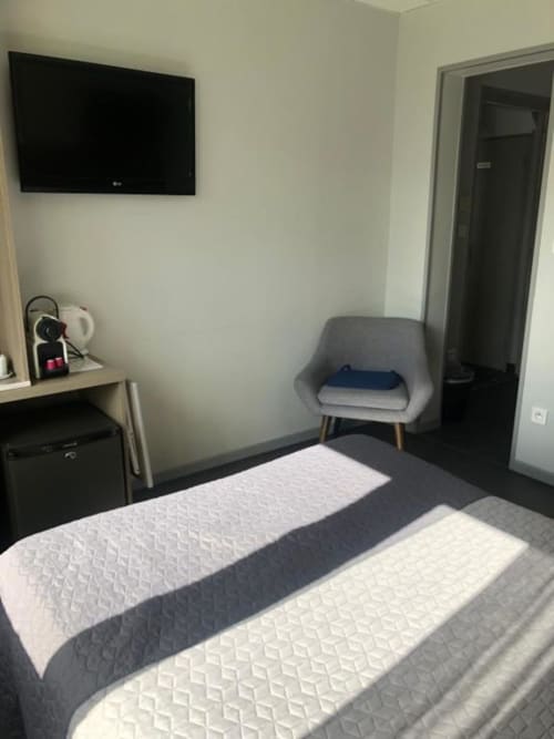Chambre double économique à l'hôtel Cosyade à Bourbourg avec lits, téléviseur mural, bureau, fauteuil gris et porte foncée
