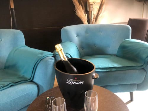 Cosyade hotel lounge with turquoise chairs, Champagne Lenson bottle in ice bucket, and glasses on wooden table