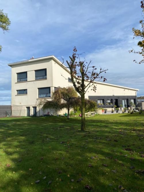 Cosyade hotel in Bourbourg, France - Modern white building with green lawn and bare tree in front yard