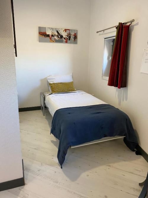 Cozy single bed in Family Studio at Cosyade hotel, Bourbourg with wooden floors and red curtains