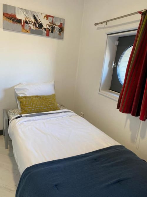 Cozy single bed in Cosyade Family Studio apartment, Bourbourg with white linens, yellow pillow, dark throw blanket, and red