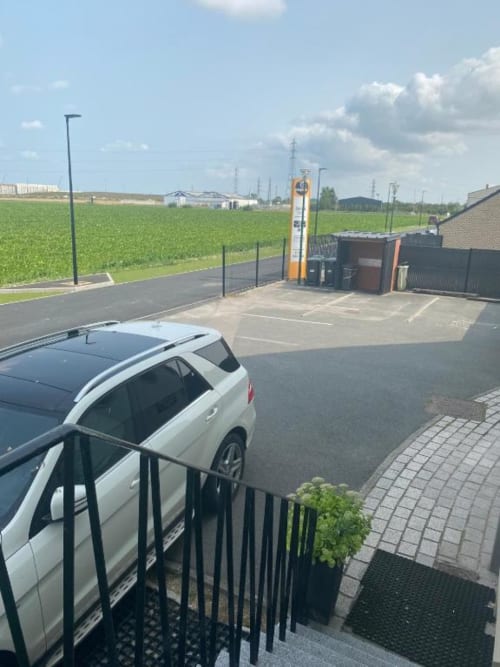 Cosyade hotel parking area in Bourbourg with white car, yellow charging station, green fields, and brick building