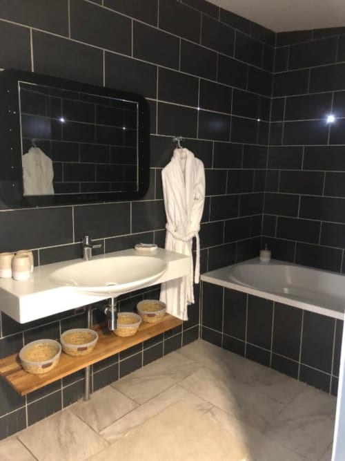 Modern bathroom in Cosyade Family Studio apartment, Bourbourg, with black subway tiles, white sink, bathtub, and wooden