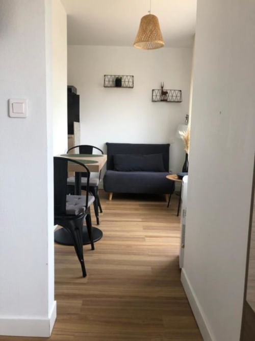Studio Supérieur moderne à l'hôtel Cosyade à Bourbourg avec canapé noir, coin repas, parquets et lampe suspendue tressée.