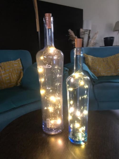 Two wine bottles filled with warm white LED lights on a dark wooden table in a Cosyade Family Studio apartment lounge area