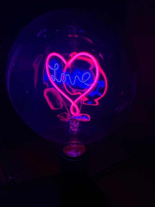 Neon heart-shaped sign with 'Love' text in pink and blue glow, romantic apartment decor at Love Room Vannes
