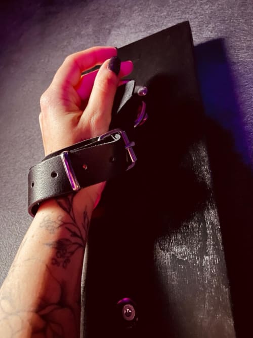 Hand holding black leather cuff with purple accents in romantic apartment at Love Room - Le Lien 56, Vannes