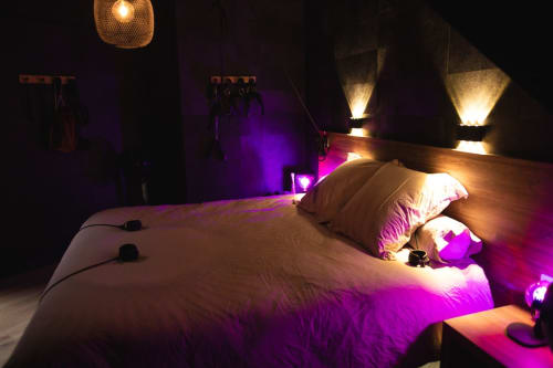 Modern romantic bedroom with ambient purple and gold lighting, bed with white pillows, wooden headboard, and decorative