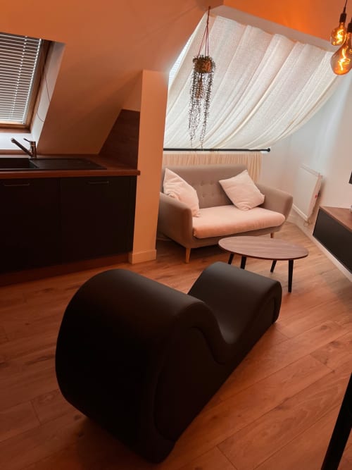 Modern apartment living room in Vannes with beige sofa, black sculptural chair, wooden floors, and sloped ceiling with