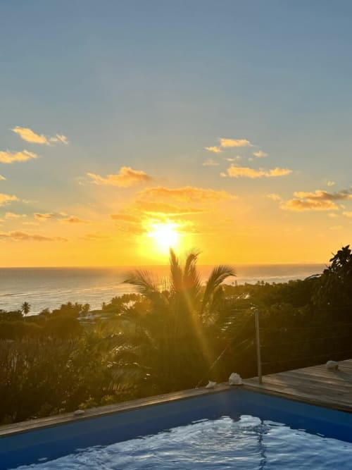 Vue du coucher de soleil depuis la piscine de Chez Marie et Philippe, Marie-Galante, avec palmiers et horizon océanique