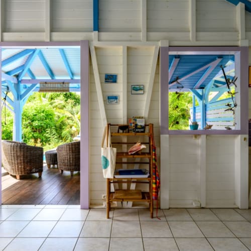 Lumineux couloir intérieur de Chez Marie et Philippe à Marie-Galante avec escalier en bois, poutres bleues et vue sur le jardin luxuriant