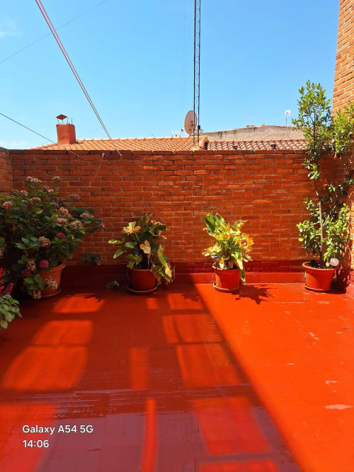 Sunny terrace with red-painted floor, potted plants, and brick wall at Benavente vacation rental