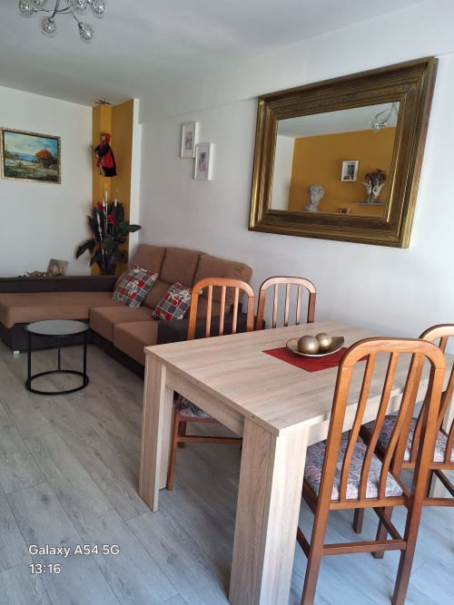 Modern living and dining area in Benavente tourist apartment with wooden table, chairs, brown sofa, and decorative mirror