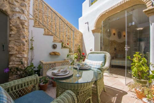 Encantador comedor en el patio de Casa La Muralla en Medina Sidonia con muebles de mimbre, muros de piedra y entrada con arco