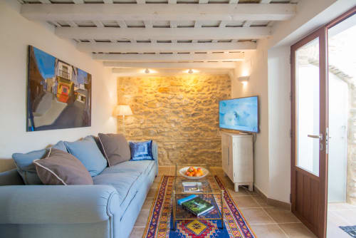 Acogedora sala de estar en Casa La Muralla con sofá azul, pared de piedra, televisor y alfombra colorida en Medina Sidonia